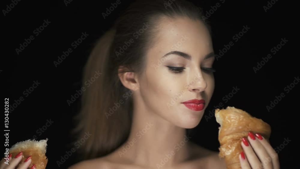Smiling young woman breaking croissant in half and smelling it Smiling young woman breaking croissant in half and smelling it