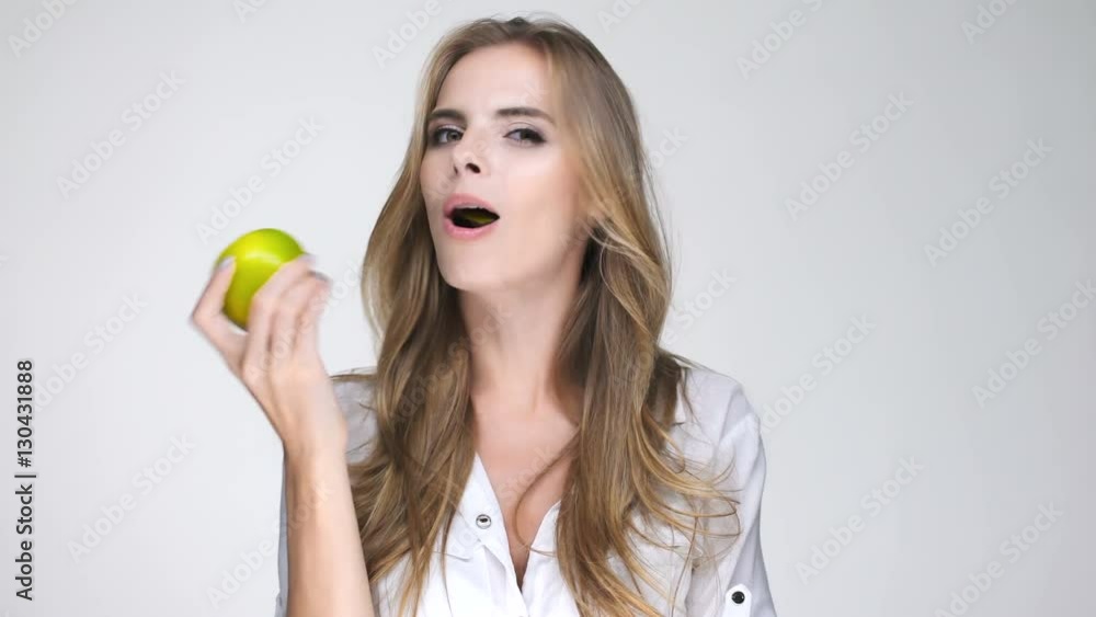 Smiling attractive woman in white shirt eating green apple Smiling attractive woman in white shirt eating green apple