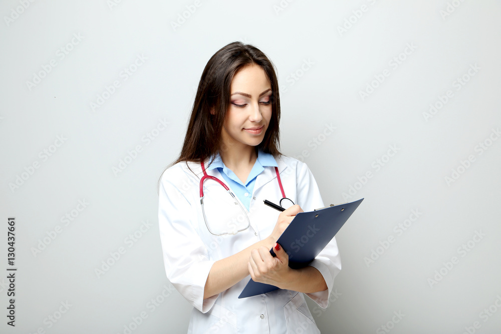 Portrait of young medical doctor with clipboard on a grey backgr Portrait of young medical doctor with clipboard on a grey backgr