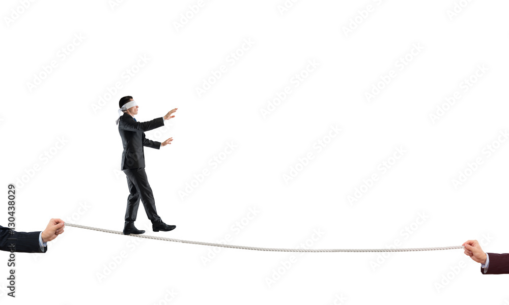 Young businessman in blindfold against white background walking on rope
