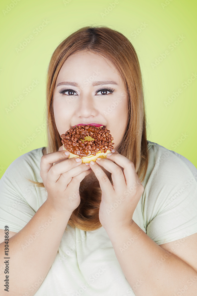 Overweight woman eating donut in hand
