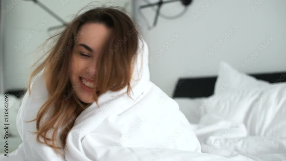 Smiling cheerful woman peeking out from under the blanket in bed at home and kissing camera Smiling cheerful woman peeking out from under the blanket in bed at home and kissing camera