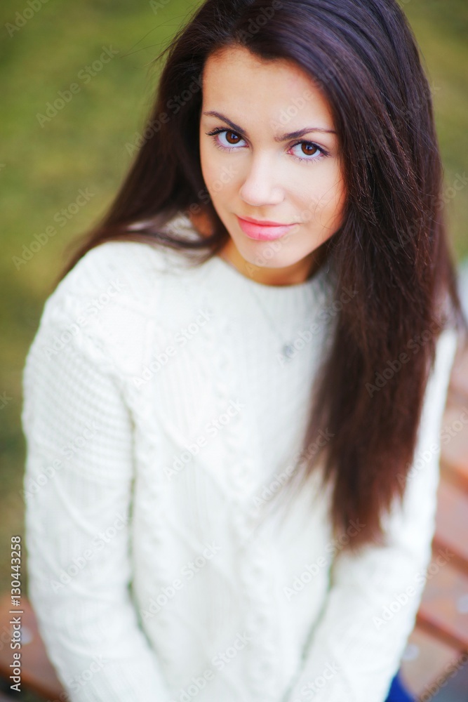 Young beautiful brown-eyed brunette girl in white sweater in the Park on blurred background , close up Young beautiful brown-eyed brunette girl in white sweater in the Park on blurred background , close up