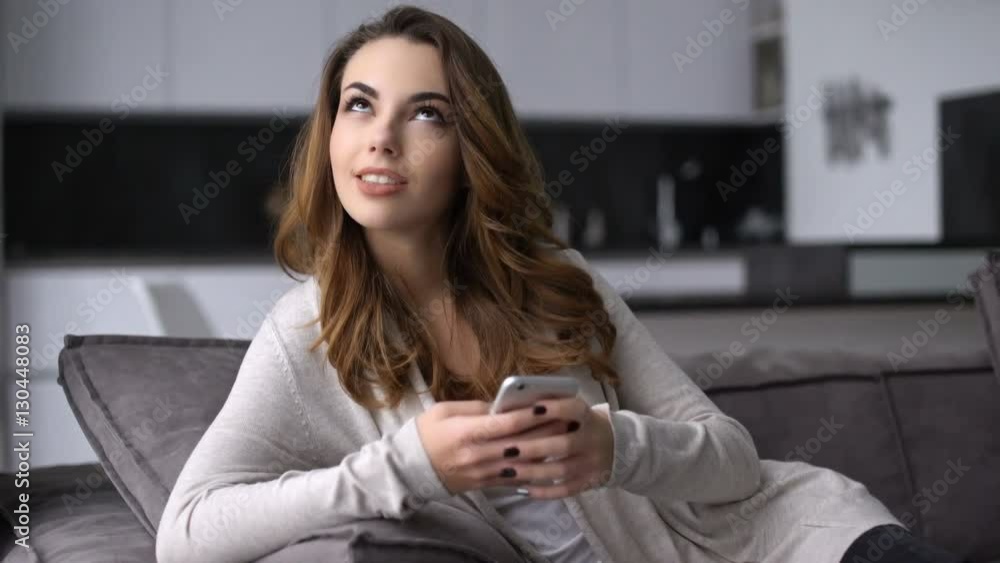 Happy smiling young girl texting message on mobile phone while sitting on a couch at home Happy smiling young girl texting message on mobile phone while sitting on a couch at home