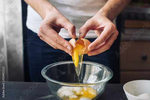 The man breaks the egg into a glass bowl