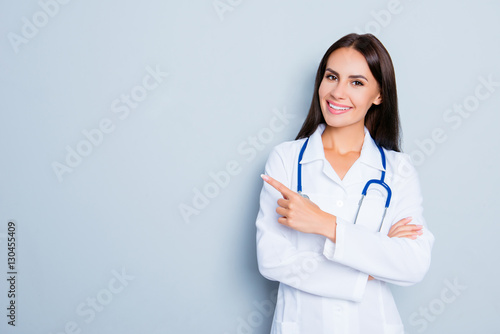 Slika na platnu Smiling happy doctor pointing with finger on blue background