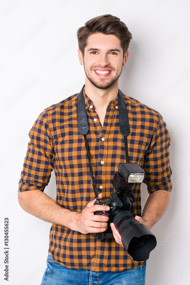 Portrait of young handsome cheerful photographer holding camera - obrazy, fototapety, plakaty 