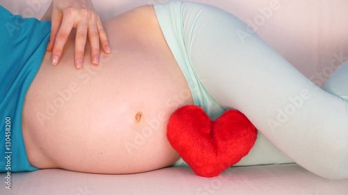 Wallpaper Mural Pregnant woman future mother lying on couch with red heart love symbol, caressing her naked belly. Pregnancy, motherhood and baby anticipation concept. 4K ProRes HQ codec Torontodigital.ca