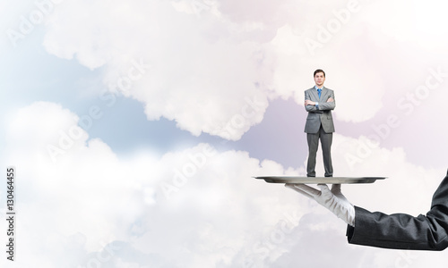 Confident businessman presented on metal tray against blue sky background
