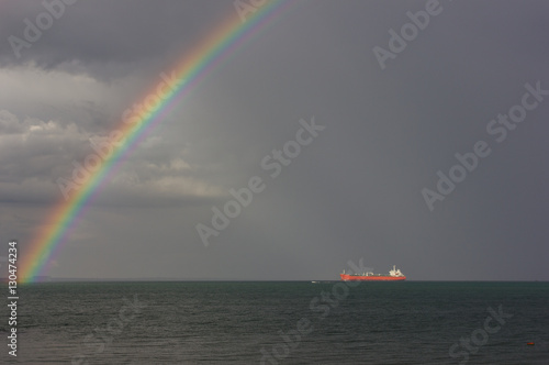 Rainbow over the sea. The sun's rays illuminate the ship. Rainbow over the ship at sea.