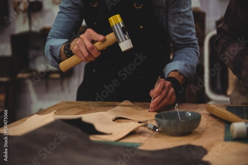 Mid-section of craftswoman hammering leather photo