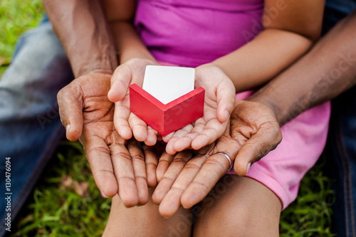 Hands of family together holding house in green park - family house concept