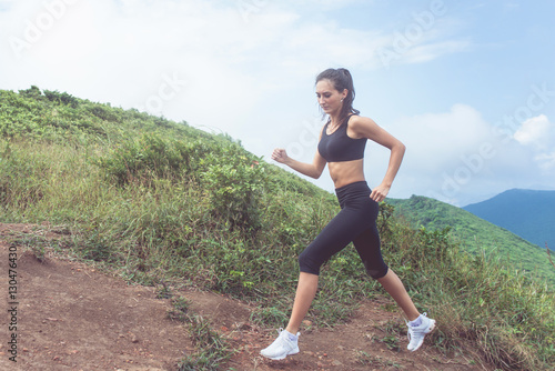 Cross-country female runner trail running on mountain path in summer. Woman wearing black sportswear exercising outdoors in wild nature