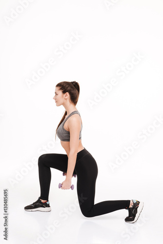 Portrait of a young pretty sportswoman doing squats with dumbbells