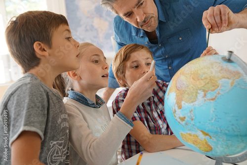 Valokuva Teacher with kids in geography class looking at globe