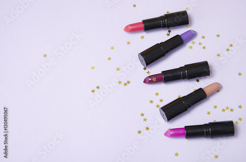 Assorted color lip stick make up on a pastel purple background with gold glittery stars and blank space at side