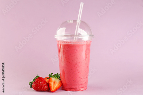 Delicious strawberry milkshake in plastic cup on pink background