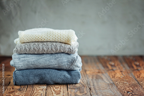 Stack of knitted winter clothes on wooden background, sweaters, space for text. Toning image photo