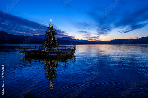 Christmas tree floating on a lake after sunset.