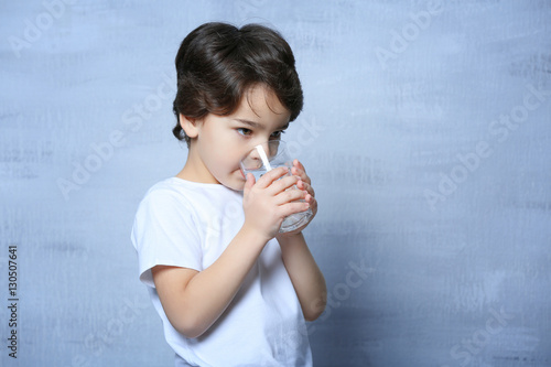 Cute little boy drinking water from glass on light blurred background