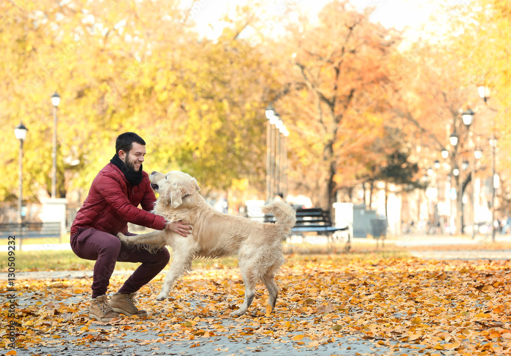 Young man playing with funny labrador retriever in autumn park Young man playing with funny labrador retriever in autumn park