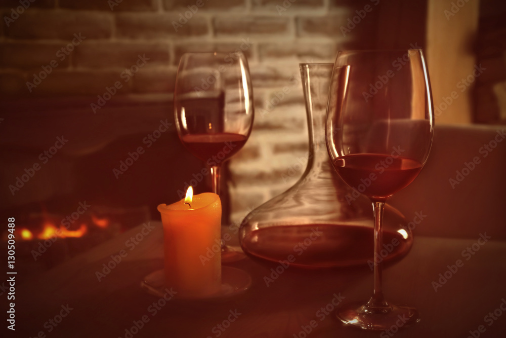 Decanter, glasses with red wine and candle on wooden table against fireplace Decanter, glasses with red wine and candle on wooden table against fireplace