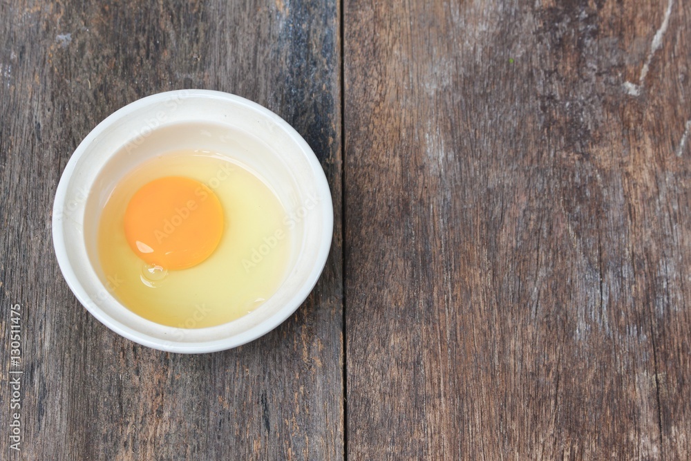 Raw egg in a bowl selective focus on wooden table Raw egg in a bowl selective focus on wooden table