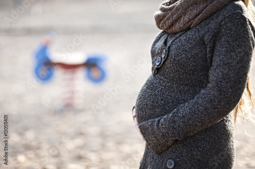 Junge Frau mit Babybauch in herbstlicher Spielplatzszenerie