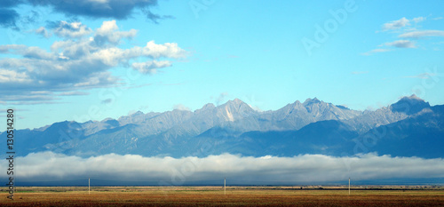Autumn Blue sky and cumulus clouds over the Eastern Sayan Mountains and Mount MunKu-Sardyk. Photo partially tinted. 