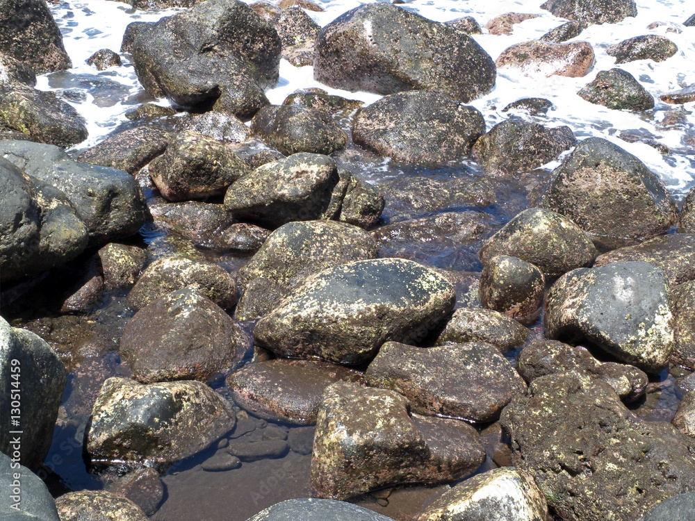 The waterworn black volcanic stones and sea water on the beach on the Ternate island, Indonesia.