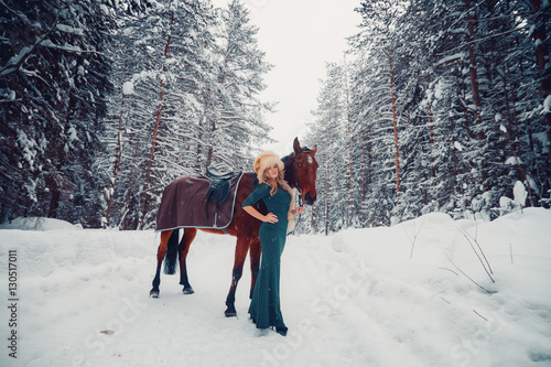 Photo Full-length of a beautiful girl in green dress in cap from the fox, and horse in the winter on the nature