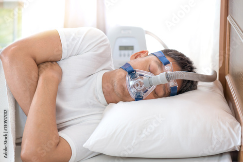 Man sleeping in bed wearing CPAP mask ,sleep apnea therapy.Happy and healthy senior man sleeping deeply on his left side without snoring photo
