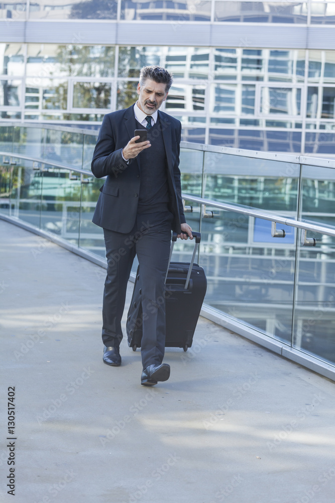 Businessman with cell phone walking with suitcase on bridge Businessman with cell phone walking with suitcase on bridge