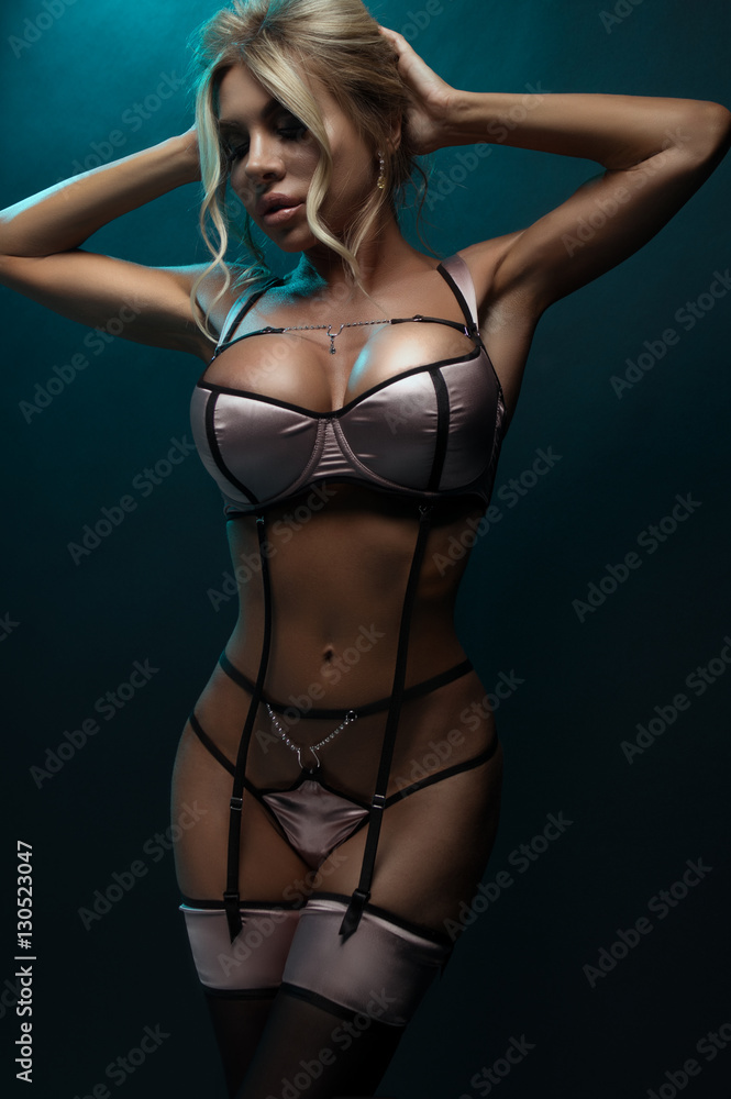 Young blonde woman in sexy lingerie on dark background with turquoise light. Young blonde woman in sexy lingerie on dark background with turquoise light.