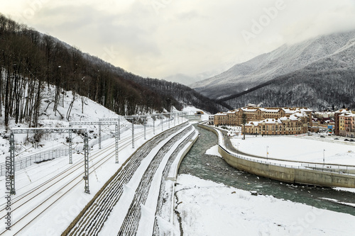 Snowy winter scenic landscape of Gorky Gorod mountain ski resort featuring a mountain river and a railway track