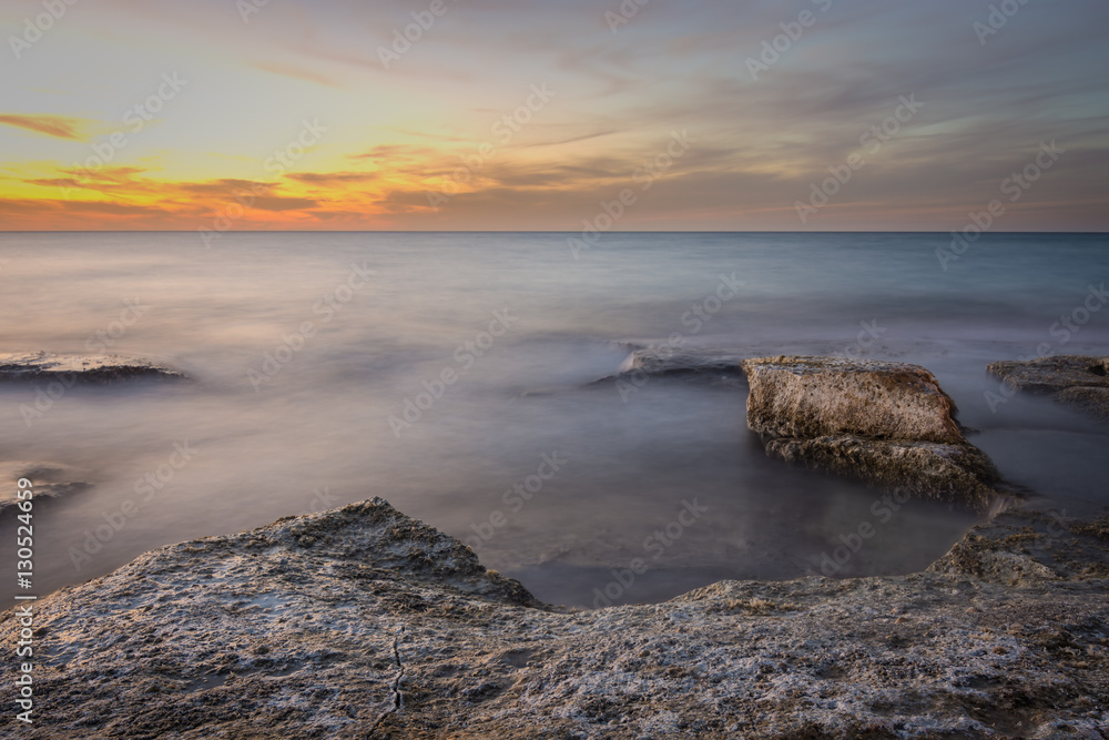 Rocks surrounded by silky waves water after a vivid sunset
