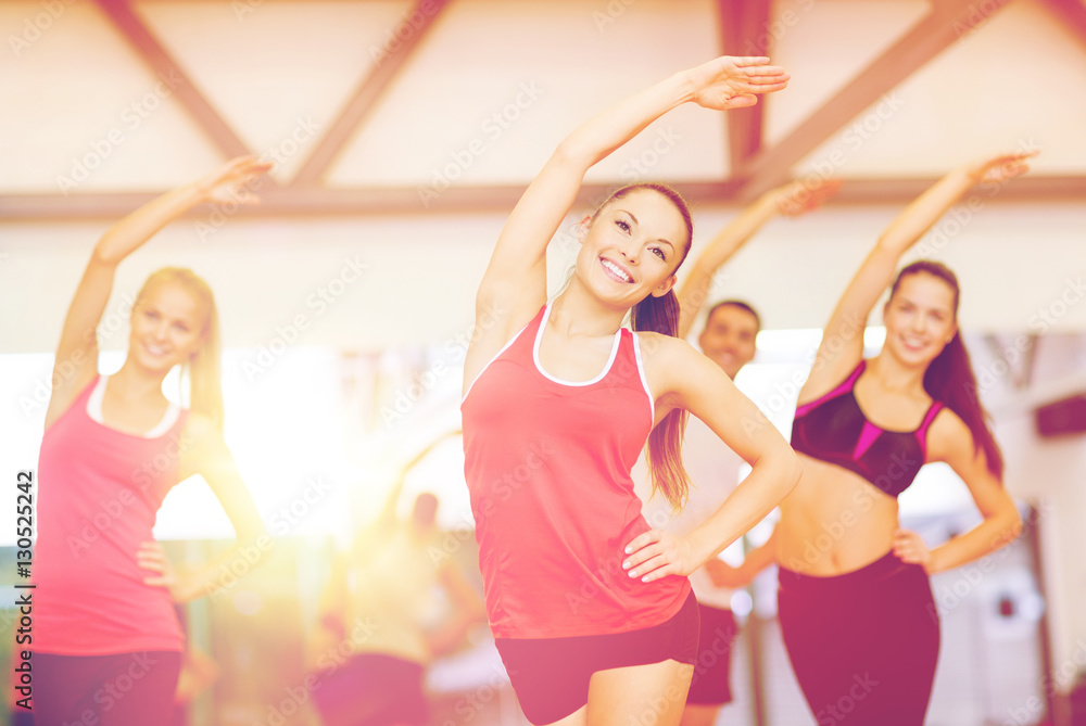 group of smiling people stretching in the gym