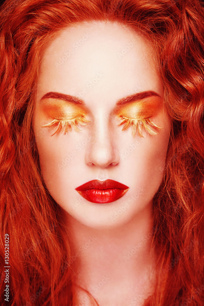 Portrait of young beautiful redhead woman with fancy feather false eyelashes and red lipstick