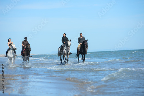 group of people on vacation riding horses on the beach in a sunny summer day