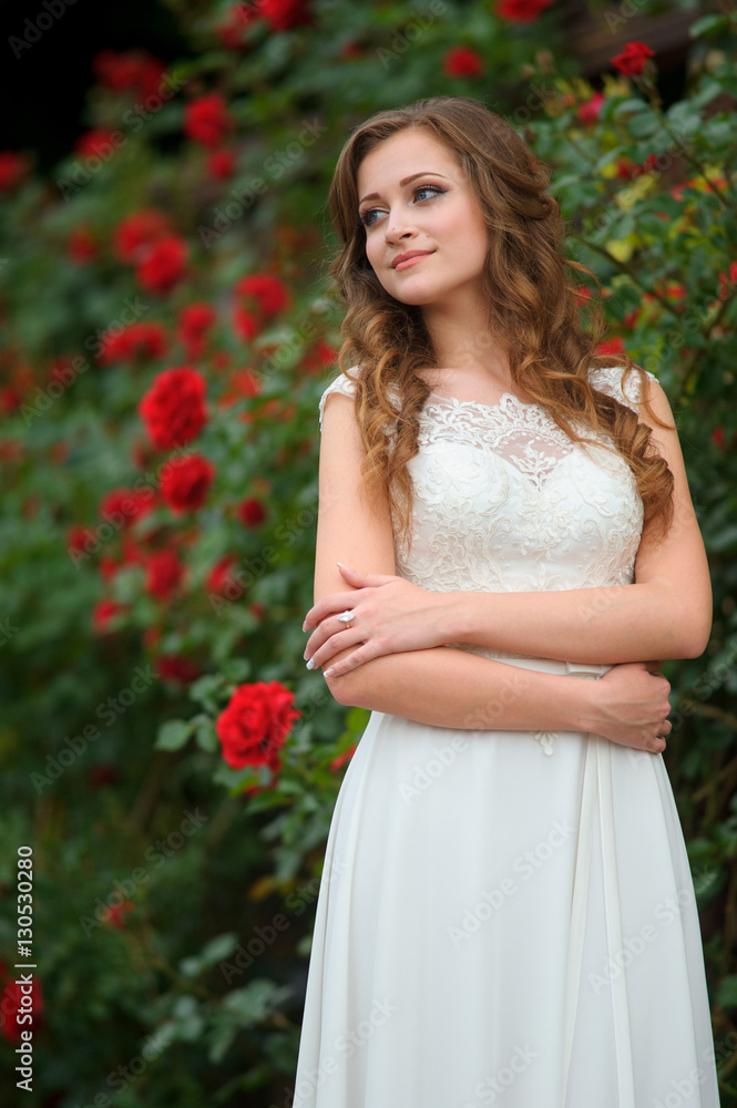 Beautiful brunette woman posing in a garden park in white long dress
