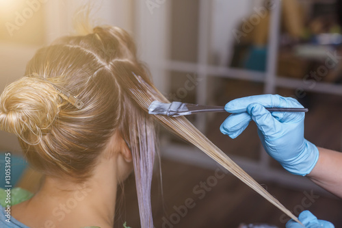 Professional hairdresser dyeing hair of her client in salon. Selective focus.