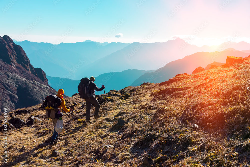 Hikers with Backpacks walking in Mountains towards rising Sun