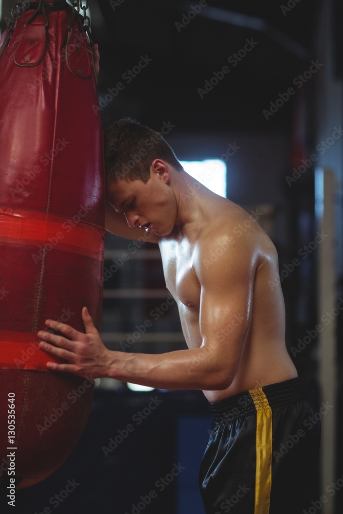 Tired boxer leaning on punching bag