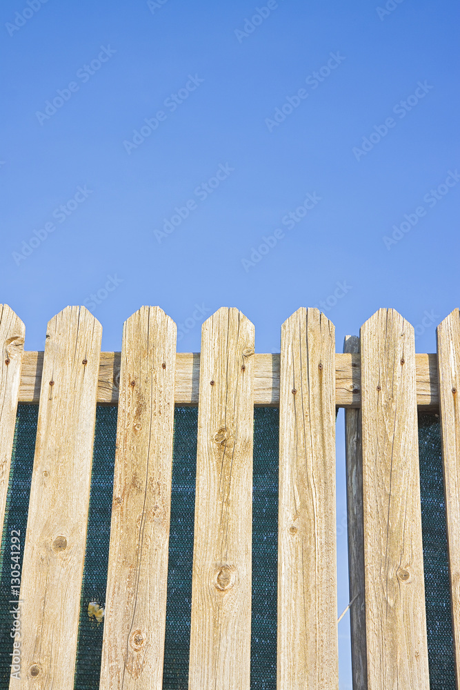 Detail of a wooden fence built with spiky wooden boards against a blue sky