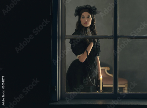 Vintage victorian woman in black dress standing behind window wi