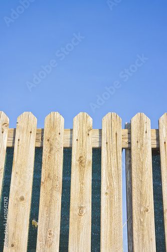 Detail of a wooden fence built with spiky wooden boards against a blue sky