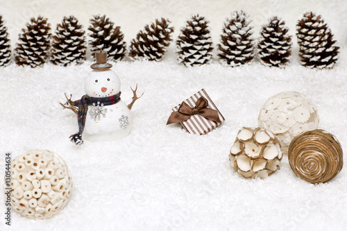 Gift box and snowman are in the snow. Christmas light background has cones. 