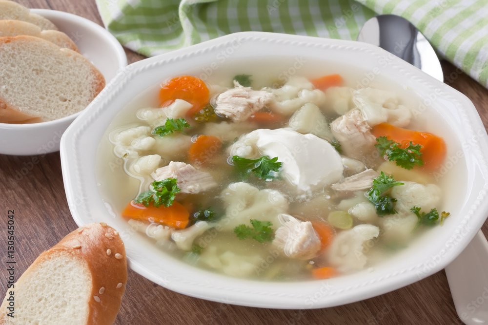 Soup with chicken, cauliflower, vegetable and bread in white plate / Vegetable soup with chicken, cauliflower, carrot, potato, parsley, cream and slice white bread in plate on wooden background Soup with chicken, cauliflower, vegetable and bread in white plate / Vegetable soup with chicken, cauliflower, carrot, potato, parsley, cream and slice white bread in plate on wooden background