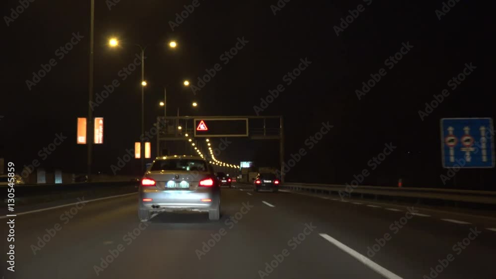 Cars go on three-lane road where is a lights billboard at night Cars go on three-lane road where is a lights billboard at night