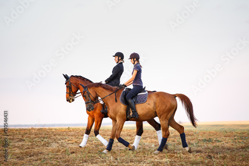 two womans ride horses on the field.